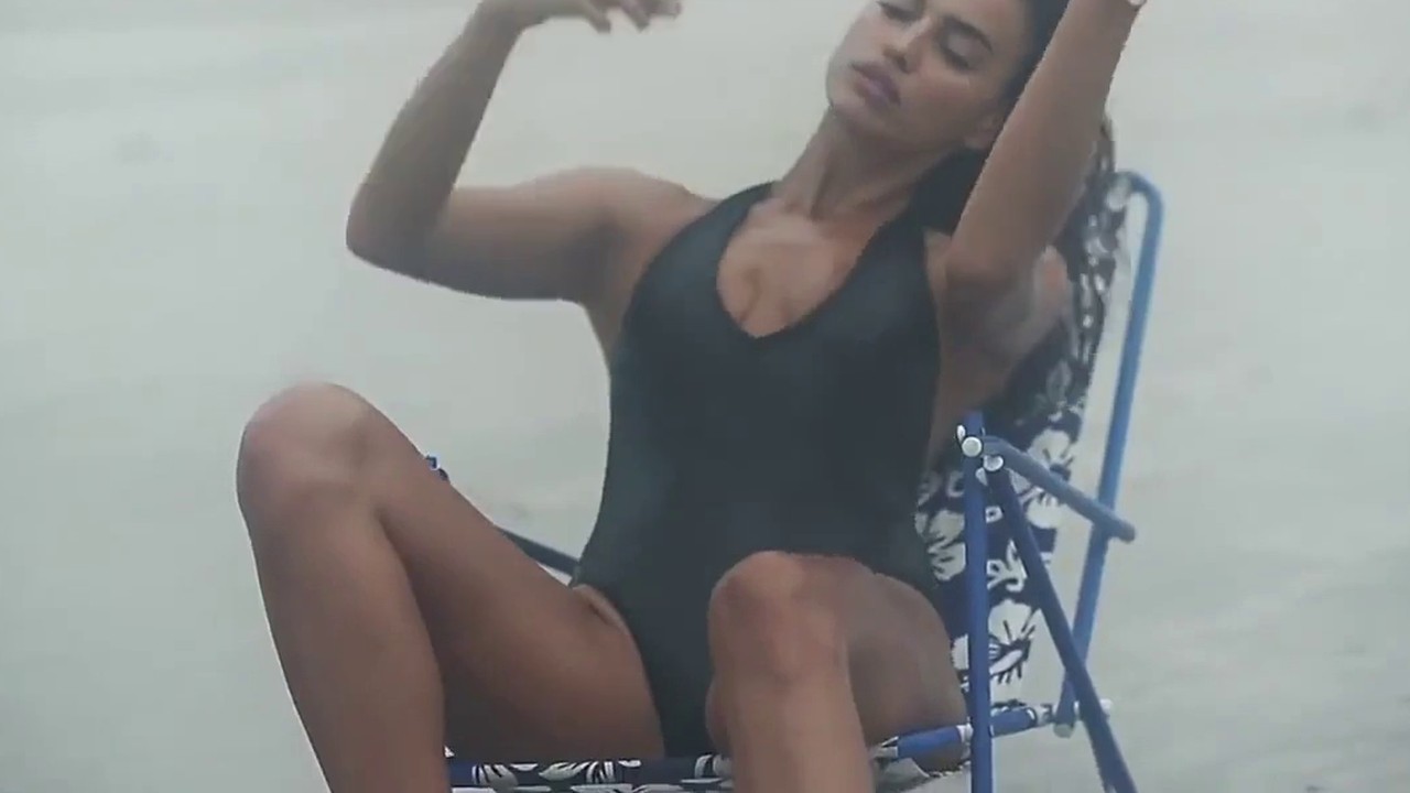Irina Shayk in a black swimsuit on a folding beach chair in the LOVE Advent 2015 video