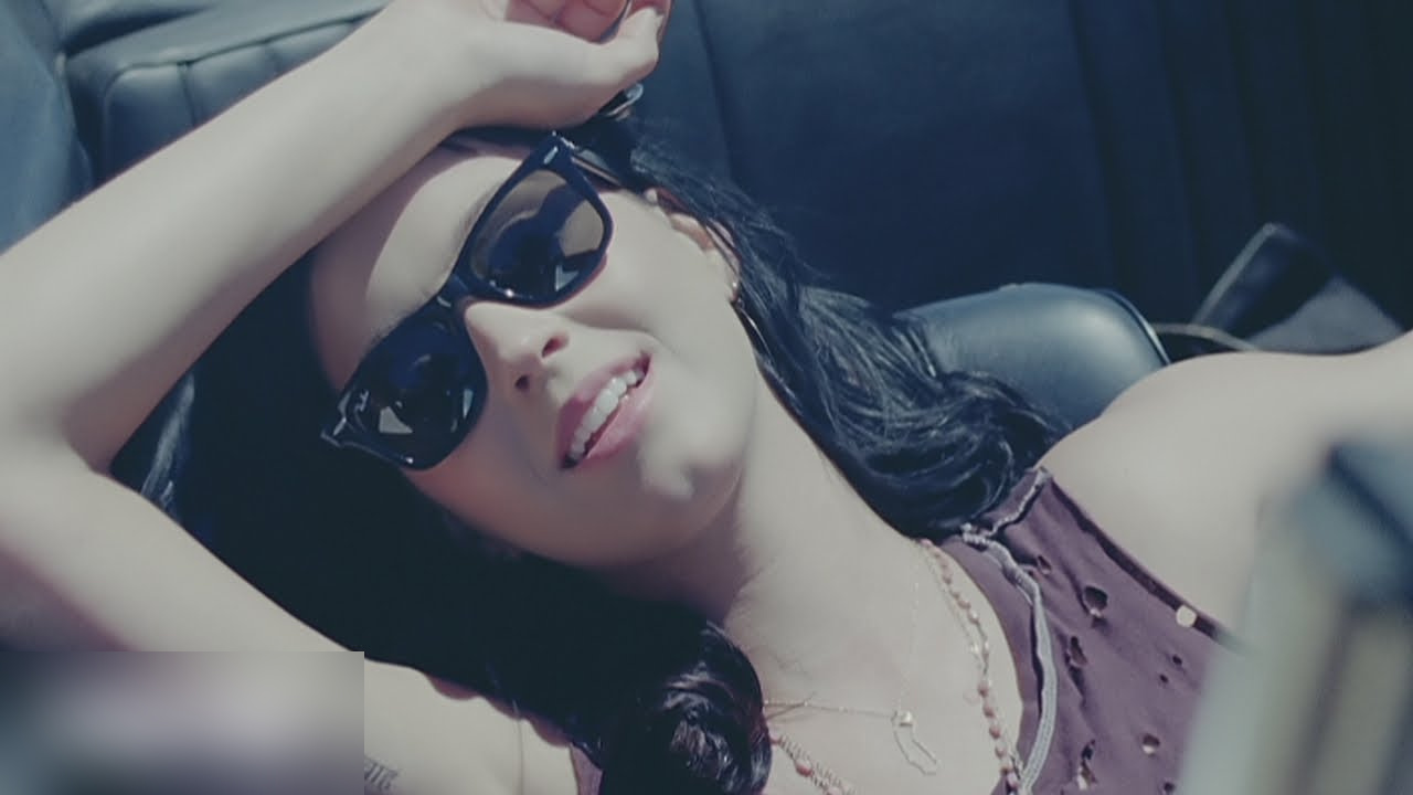 Katy Perry in sunglasses and a lace top leaning back in a car seat, Teenage Dream video (2010)