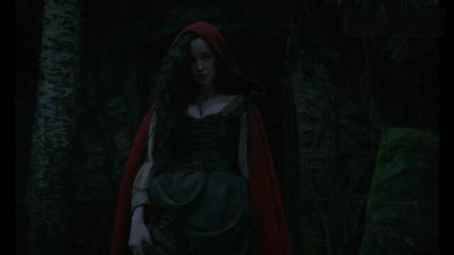 Sarah Stephens as the young witch, in a red hood outside a hut in The Witch